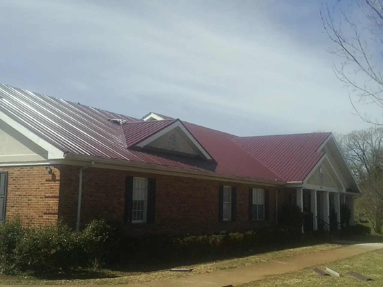 Red metal roof with gabled entries on a long brick building, from a Hail Damage Roof Repair job in Opa Locka