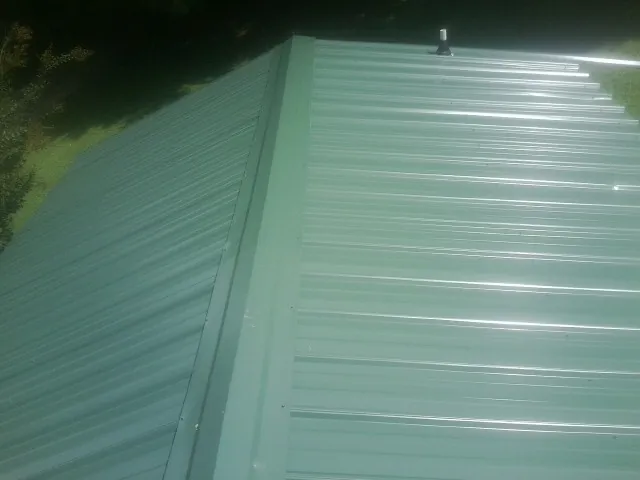New green metal panels meeting at the ridge of a roof — Flat Roof Repair work by our crew in Opa Locka