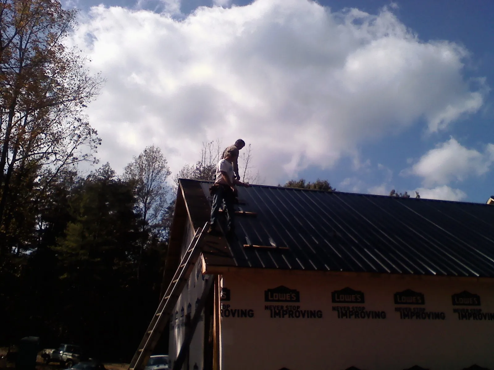 Roofer fastening dark metal panels high against a cloudy sky, from a Roof Inspection job in Opa Locka