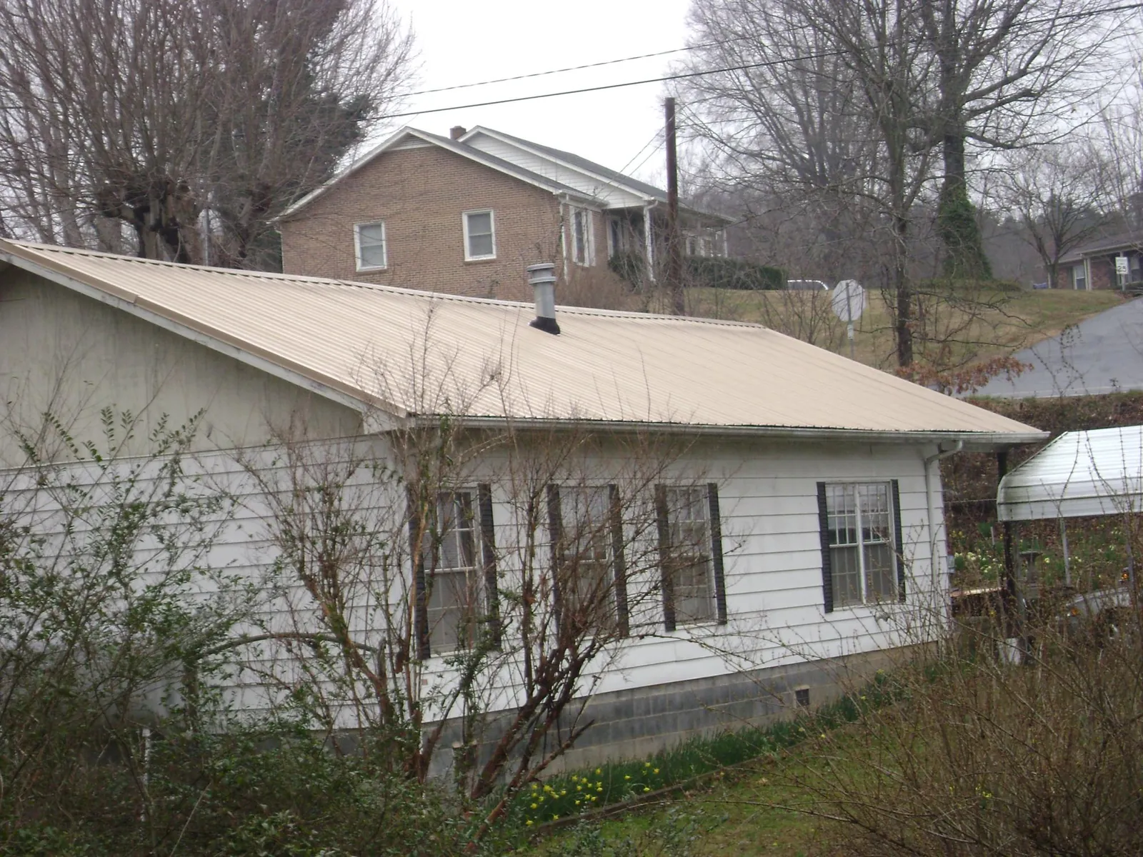 Tan metal roof on a white sided house set into a hillside — Commercial Roofing by Roofing Brothers in Opa Locka
